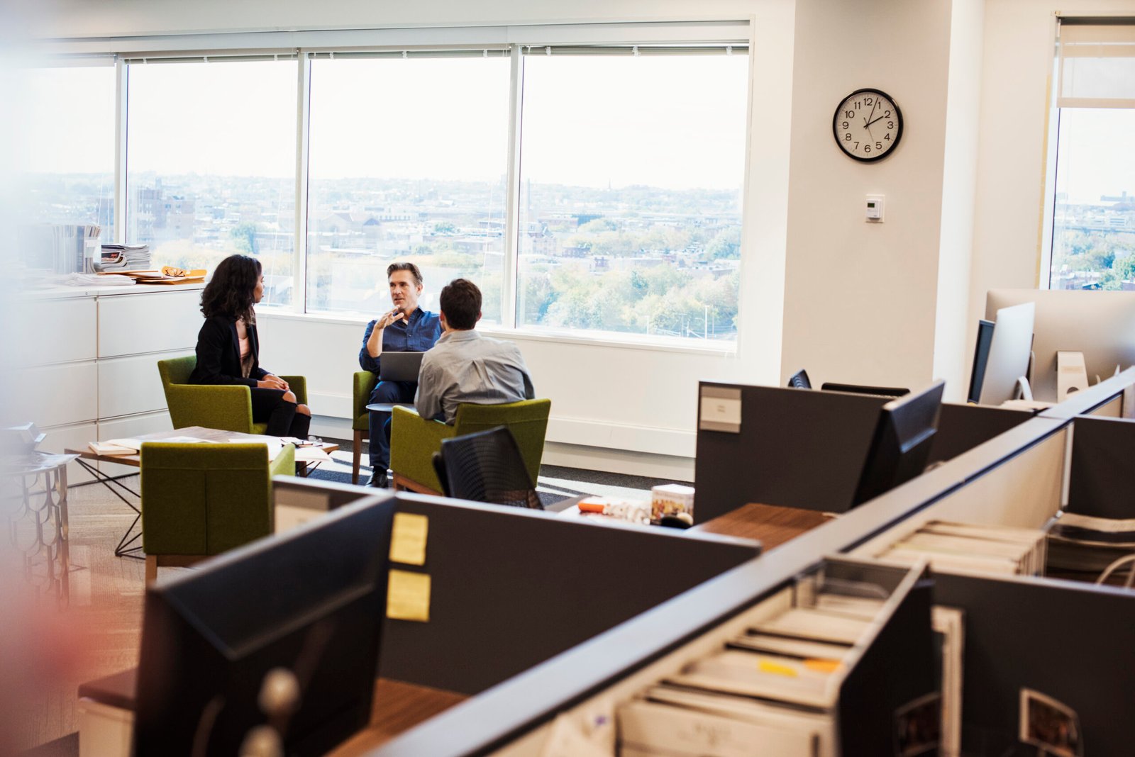 A woman and two men sitting in armchairs in an office talking to each other.