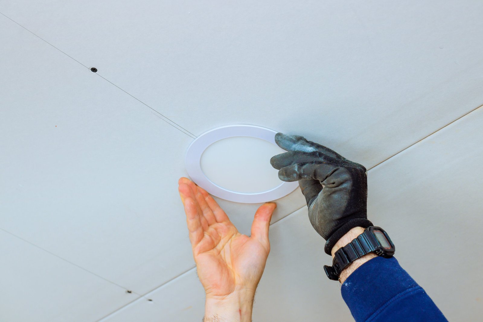Worker adjusts circular ceiling light fixture in contemporary room, at during home improvement